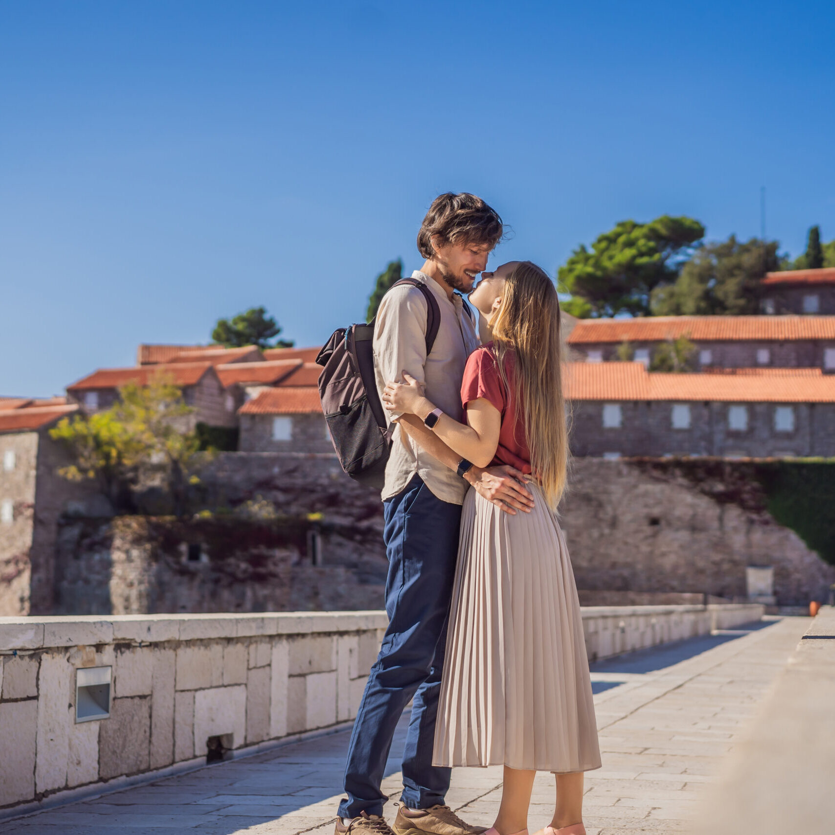 Man and woman tourists on background of beautiful view of the island of St. Stephen, Sveti Stefan on the Budva Riviera, Budva, Montenegro. Travel to Montenegro concept Man and woman tourists on background of beautiful view of the island of St. Stephen, Sveti Stefan on the Budva Riviera, Budva, Montenegro. Travel to Montenegro concept.